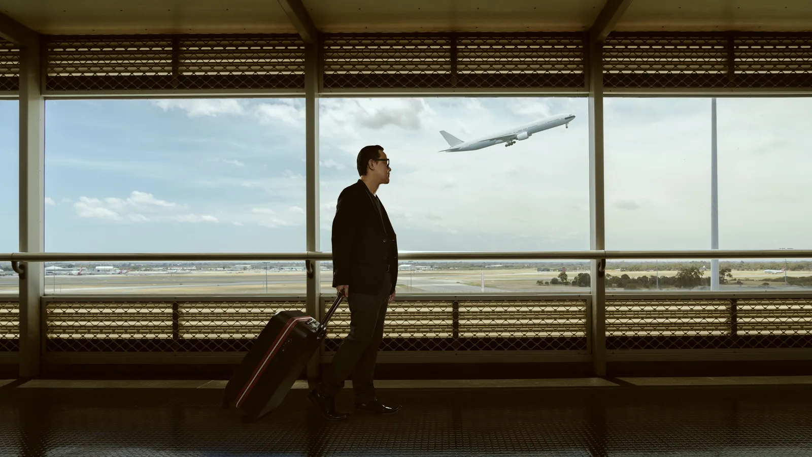 Silhouetted traveler with rolling suitcase at airport window